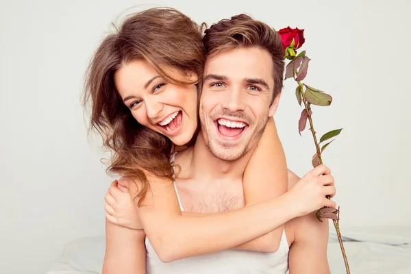 Alegre jovem casal apaixonado abraçando no quarto com rosa — Fotografia de Stock