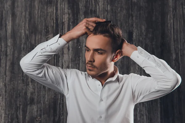 Attractive rigid man combing hair on the grey background — Stock Photo, Image