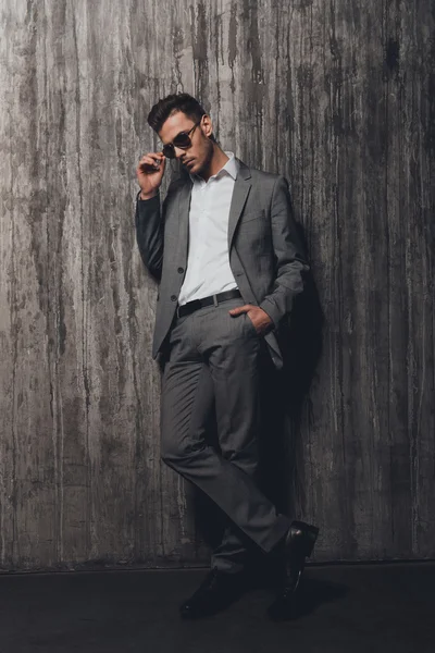 Elegante hombre con gafas cogidas de la mano en un bolsillo en la ba gris — Foto de Stock