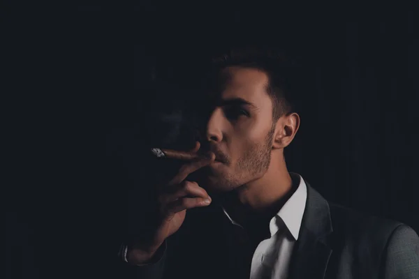 Handome confident man in suit on the black background smoking a — Stock Photo, Image