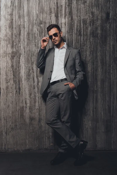 Hombre guapo con gafas cogidas de la mano en un bolsillo en el gris b — Foto de Stock