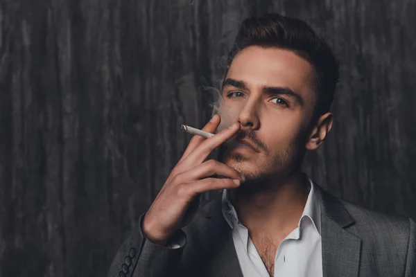 Retrato de un hombre descarado en traje sobre el fondo gris fumando —  Fotos de Stock