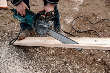 Bir işçi elektrikli testereyle tahtayı keser.