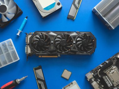 Sabit disk, ram, işlemci, grafik kartı ve anakart içeren bilgisayar parçalarının üst görünümü mavi tablo arka planında.
