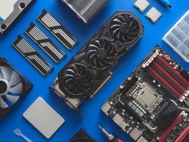 Sabit disk, ram, işlemci, grafik kartı ve anakart içeren bilgisayar parçalarının üst görünümü mavi tablo arka planında.