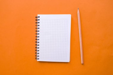 Üst görünüm not defteri ve kalem, turuncu arka planda izole edilmiş. Uzayı kopyala, düz yat.