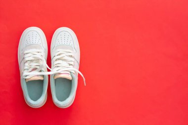 Kırmızı arka planda izole edilmiş beyaz spor ayakkabılar. Üst Manzara. Düz yatıyordu. Spor kıyafetleri. Bir çift kadın ayakkabısı..