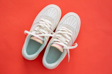 Bir çift kadın ayakkabısı. Kırmızı arka planda beyaz spor ayakkabılar var. Düz yatıyordu. Üst görünüm.