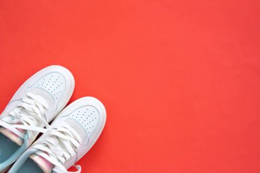 Kırmızı arka planda izole edilmiş beyaz spor ayakkabılar. Üst Manzara. Düz yatıyordu. Spor kıyafetleri. Bir çift kadın ayakkabısı..