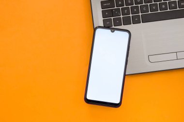 Not defterinin klavyesinde beyaz ekran olan akıllı telefon. Model telefon. Üst Manzara. Düz yatıyordu. Turuncu arkaplanda kopyalama alanı ile izole edilmiş.