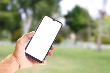 Elinizde boş beyaz ekran telefonu, arka planda bulanık doğa görüntüsü, kırpma yolu, kopyalama alanı, taklit resim.