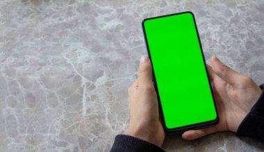 Mermer masa arka planında yeşil ekran cep telefonu kullanan bir kadının görüntüsü. Üst görünüm, alanı kopyala.