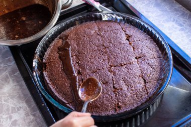 Genç bir kadın ev yapımı kekin üzerine çikolata kreması döküyor. Ev yapımı tatlılar pişiriliyor.