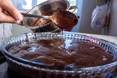 Genç bir kadın ev yapımı kekin üzerine çikolata kreması döküyor. Ev yapımı tatlılar pişiriliyor.