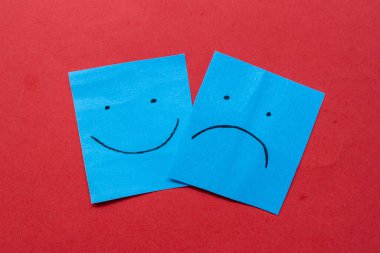 Çıkartmalarda mutlu ve üzgün yüz ifadesi var. Kağıda elle çizilmiş yüzler. Farklı duygular birlikte. Kırmızı arkaplanda izole.