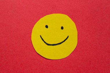 Sarı etikete el çizilmiş gülen surat. Kırmızı arkaplanda izole edilmiş kağıttaki mutlu yüz.