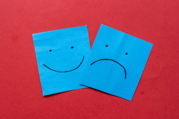 Happy and sad face on stickers. Hand drawn faces on paper. Different emotions together. Isolated on red background.