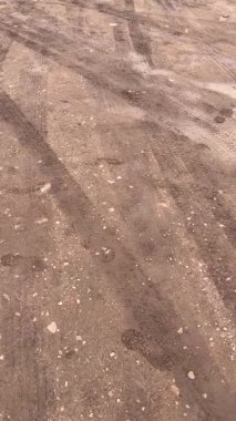 Islak toprak ve çakıl zeminde kavisli lastik izleri.