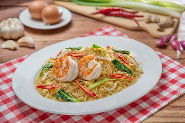Plate of fried vermicelli with shrimps and herbs on the table in
