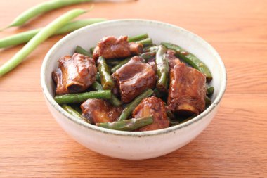 Bowl of fried pork ribs with green bean on wooden table clipart
