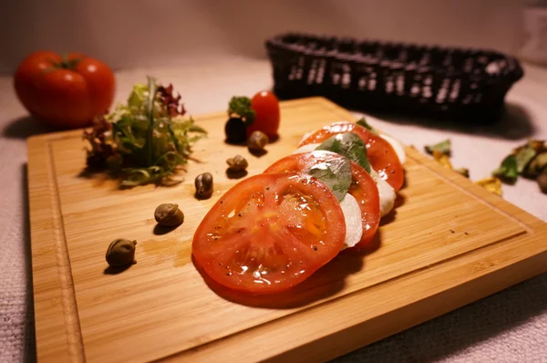 Tomate en rodajas con calamares sobre tabla de cortar de bambú sobre la mesa — Foto de Stock