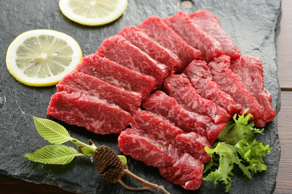 Fresh sliced beef on black rock plate with lemon and herbs — Stock Photo, Image