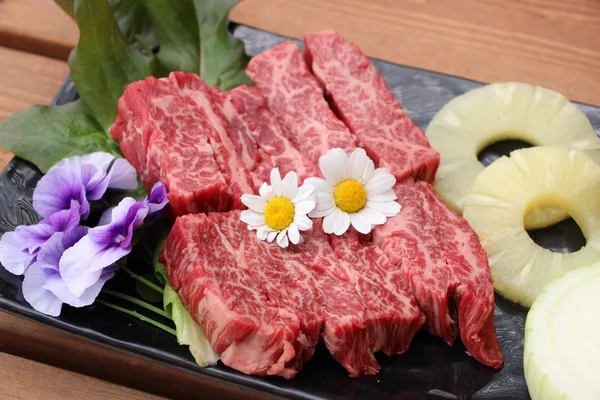 Carne roja fresca con piña en rodajas y flores en plato negro — Foto de Stock