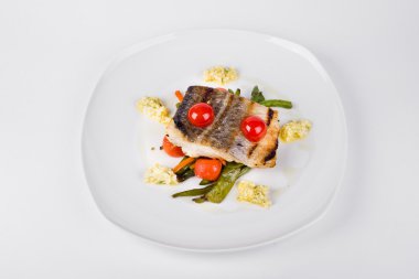 Beyaz tabakta sebze ile kızarmış morina fileto