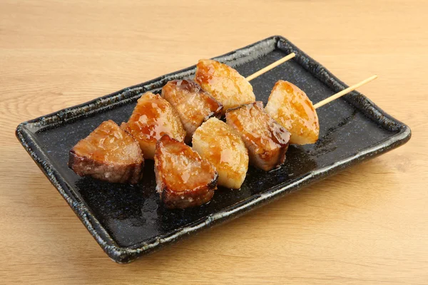 Spieße aus geröstetem Thunfisch auf schwarzem Teller auf Holztisch — Stockfoto