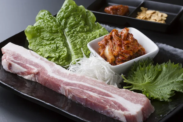 Свежая свинина с салатом и кимчи на черном блюде — стоковое фото
