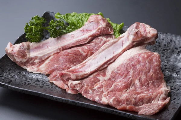 Hueso fresco en costillas de cerdo con lechuga en plato negro — Foto de Stock