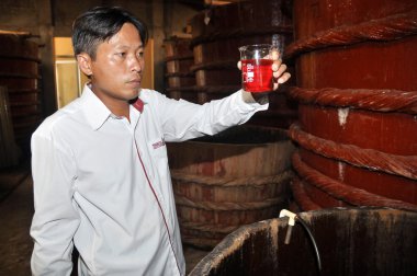 Phu Quoc, Vietnam - August 19, 2013: An expert is checking the quality of the fish sauce sample which is a traditional sauce in Vietnam, from a fermented tank in Phu Quoc island.