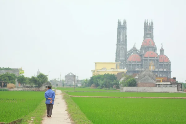 Nam Dinh, Vietnam - March 28, 2010: A farmer is walking toward a catholic church in a countryside in the North of Vietnam — Stock Photo, Image