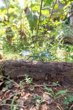 yuvarlak siyah gözlük çerçevesi eski ahşap üzerinde. Ön taraftaki fotoğrafta yuvarlak camlar ve arka tarafta doğal bir manzara var.