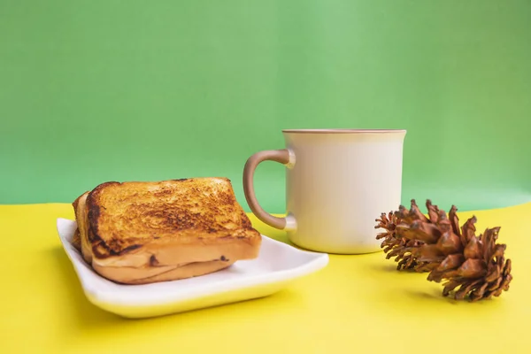 Toast On White Plate And Black Coffee Mug With Spruce Flower Decoration On Yellow And Green Paper Background. Toast And Black Coffee For Breakfast. Horizontal Phot