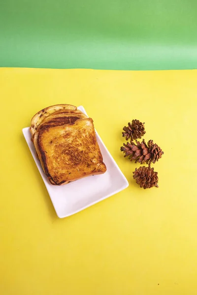 Φρυγανισμένο Ψωμί Λευκό Πιάτο Άνθη Ελάτης Κίτρινο Και Πράσινο Φόντο — Φωτογραφία Αρχείου