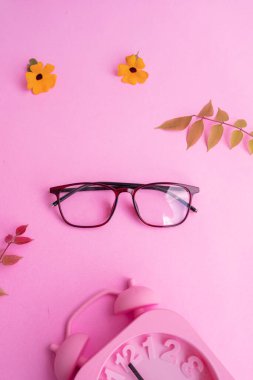 Kare gözlük, çalar saat, pastel pembe arka planda yeşil yapraklar. Yaz Konsepti, Asgari Konsept