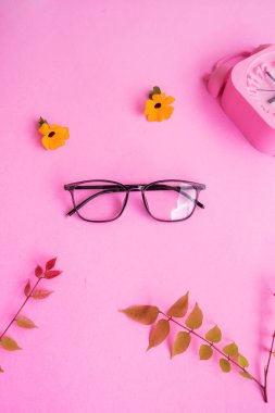 Kare gözlük, çalar saat, pastel pembe arka planda yeşil yapraklar. Yaz Konsepti, Asgari Konsept