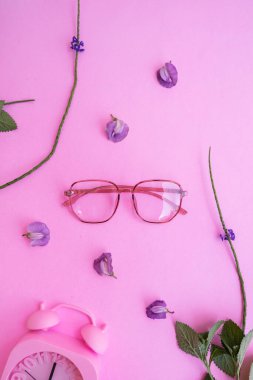 Resimde beş köşeli gözlük var. Pastel pembe arka planda, yaz tarzında. Alarmlı saat mor floş