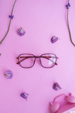 Resimde beş köşeli gözlük var. Pastel pembe arka planda, yaz tarzında. Alarmlı saat mor floş