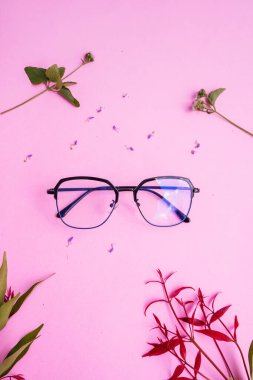 Resimde metal kare gözlük var. Pastel pembe arka planda, en az yaz tarzında. Kırmızı yaprak, yeşil yaprak, akarsu
