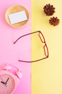 Resimde kare gözlük var. Minimum yaz tarzında. Pastel pembe ve sarı arka planda. Alarm Saati, Çam Ağacı Çiçekleri, İş Kartı