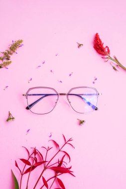 Resimde metal kare gözlük var. Pastel pembe arka planda, en az yaz tarzında. Kırmızı yaprak, yeşil yaprak, akarsu