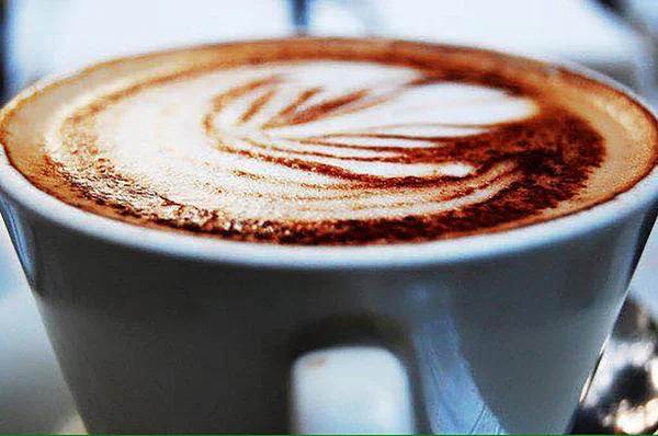 Latte sanat kahvesi beyaz bardakta, ahşap masada.