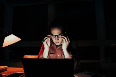 Stresli Kafkasyalı erkek, gece geç saatlere kadar dizüstü bilgisayarla çalışarak gözlük ayarlıyor. 