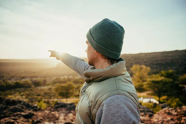 Caucasian male free spirit pointing at sunset in distance while walking in wilderness