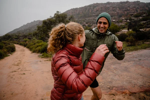 Laughing fit young couple enjoying long distance trail run on gravel mountain track in cloudy weather