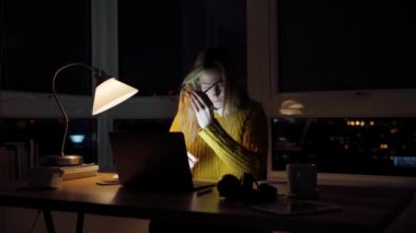 Beyaz bir kız öğrenci gece geç saatlere kadar çalışıyor. Gözlerini ovuşturuyor. Dizüstü bilgisayarda yazı yazıyor.