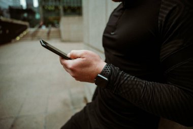 Beyaz erkek sporcu akıllı telefondan kayıyor. Açık havada koşarken etkinlik güncellemesini kontrol ediyor.