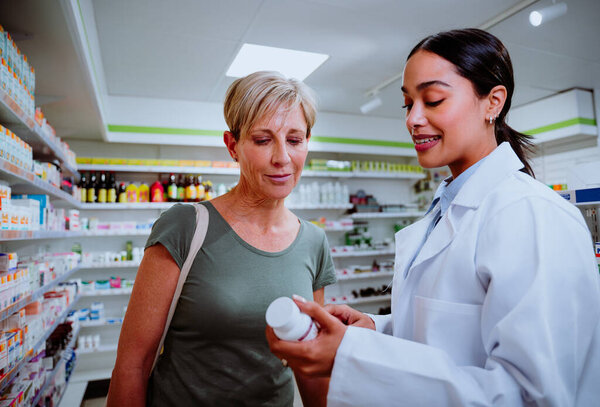 Кавказская мать получает помощь от фармацевта смешанной расы, объясняющего меры предосторожности в дозировке лекарств